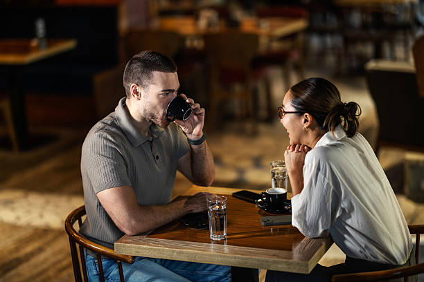 Young couple sharing laughter and coffee at a modern cafe table, enjoying relaxed conversation and warm, candid connection with each other