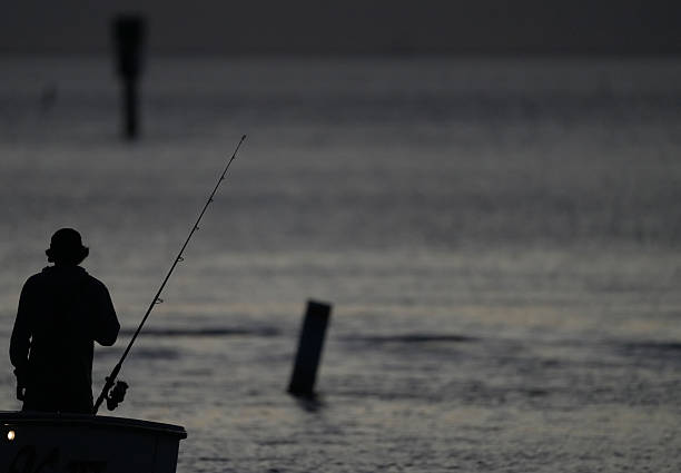 Santa Pola, Alicante, Spain- November 26, 2025: Man fishing with a rod in the port of Santa Pola at sunset