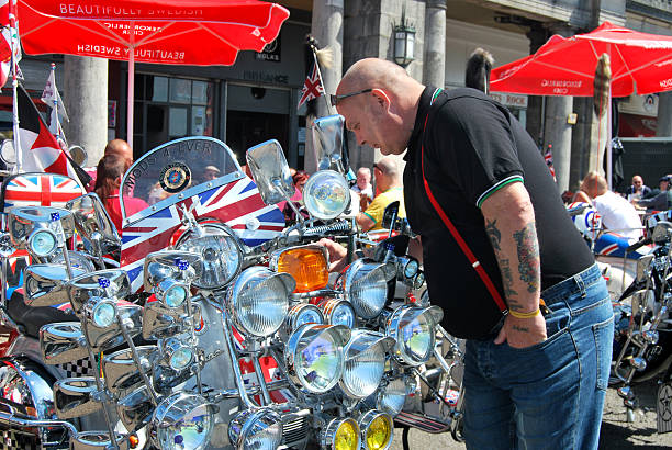 Brighton, United Kingdom - June 4th, 2017: Man at British Mod event looking at scooters adorned with chromed plated mirrors, Union Jack flags, headlights and shiny accessories