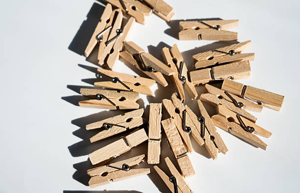Wooden clothespins scattered on a bright white background, casting distinct shadows. Representing organization, creativity, and household tasks