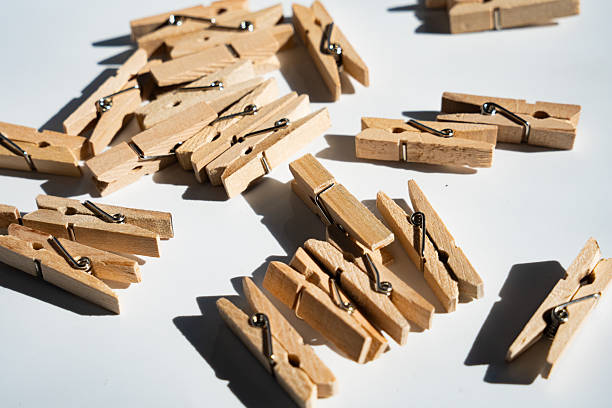 Many small wooden clothespins randomly arranged on a bright white background, creating strong, angled shadows from direct sunlight