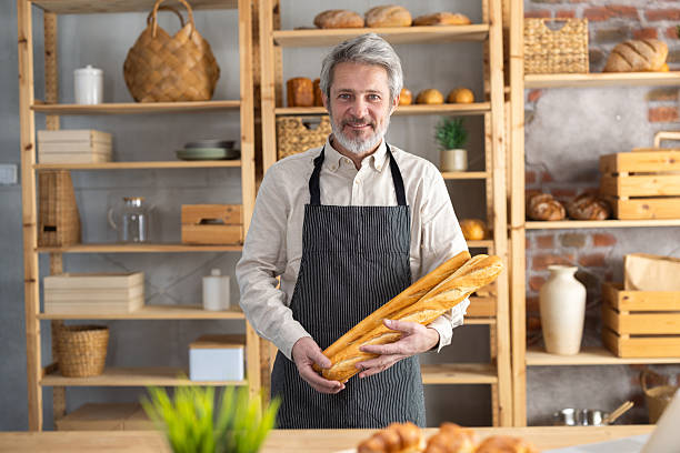 Baker holding fresh baguettes in bakery shop