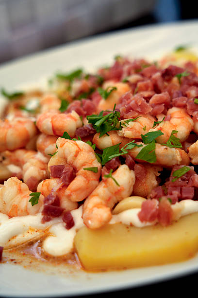 Shrimp tapas served on potatoes with ham and a white creamy sauce, garnished with parsley