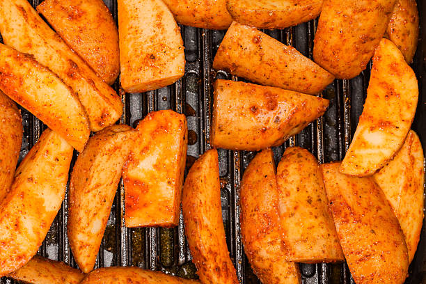 A close-up shot of golden brown potatoes sizzling on a grill, their surfaces glistening with oil and seasoned with herbs.