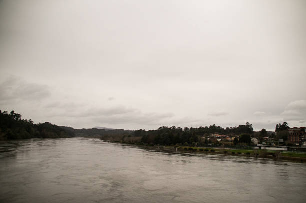 Wide shot of a powerful river breaking its banks and flooding a recreational park with tennis courts and walking paths.