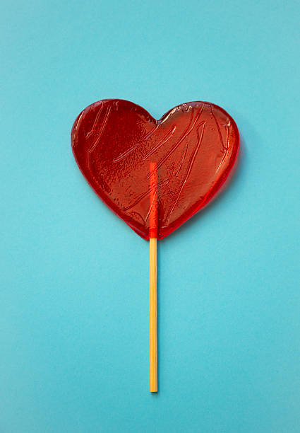 Minimal love concept with red heart shaped lollipop on bright blue background. Bold colors and clean copy space make this image ideal for Valentine advertising, social media posts and romantic promotions.