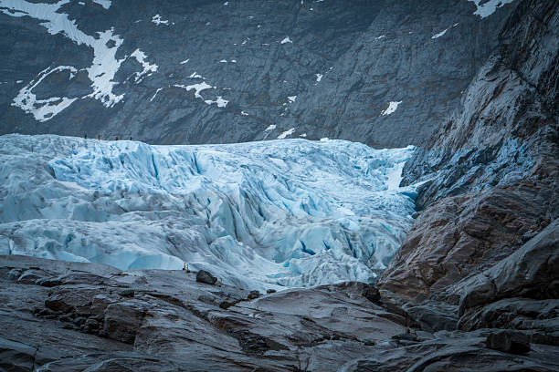 Dramatic view of Nigardsbreen glacier in Norway, showing blue ice formations, rugged rocks, and mountain landscape. Powerful symbol of climate change and raw nature.