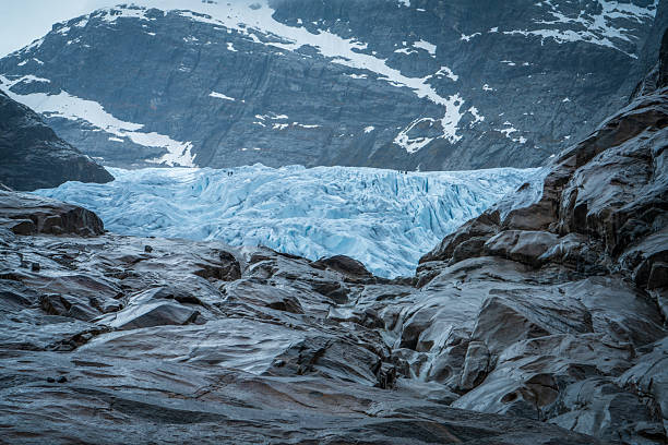 Dramatic view of Nigardsbreen glacier in Norway, showing blue ice formations, rugged rocks, and mountain landscape. Powerful symbol of climate change and raw nature.