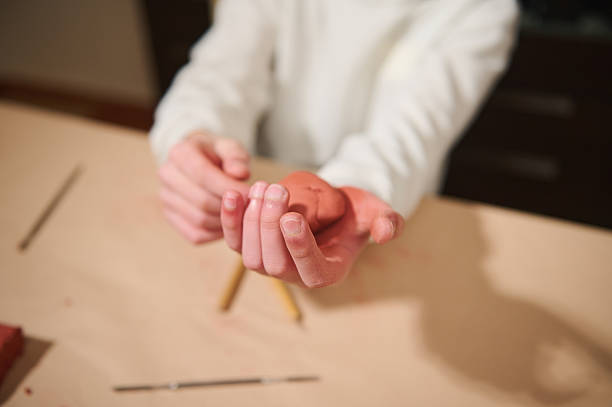 Hands of a young, multi-ethnic boy mold clay on a light table, pencils nearby. A quiet, creative moment at home, showing concentration and the joy of making art.