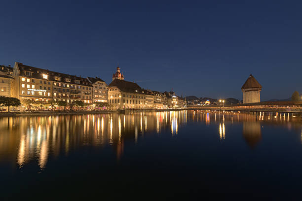 The historic Chapel Bridge and the Reuss river in Lucerne, Switzerland, are beautifully illuminated at night, creating a stunning reflection