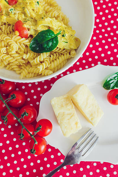 A bowl of pasta with sauce is placed next to a plate of cheese and fresh cherry tomatoes on a tablecloth.