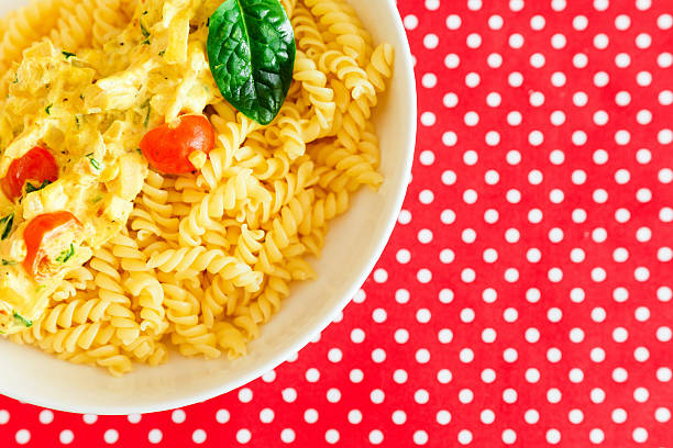 A bowl contains pasta mixed with sauce and cherry tomatoes placed on a red tablecloth with white dots.
