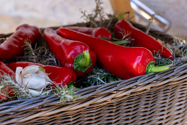 vibrant red peppers and garlic cloves rest in a wicker basket, surrounded by fragrant herbs. the natural light highlights the fresh, organic produce
