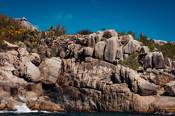 Powerful ocean waves crashing onto the unique granite rock formations and tropical vegetation along the natural coastline of La Digue island in Seychelles