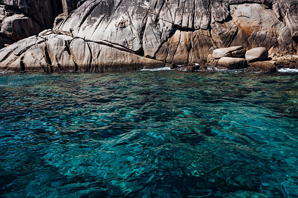 Crystal clear turquoise ocean water gently lapping against ancient weathered granite rock formations, showcasing the unique geological beauty and serene tropical nature of the Seychelles islands