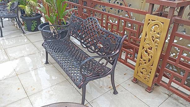 Black metal bench on a patio with red railing and potted plants
