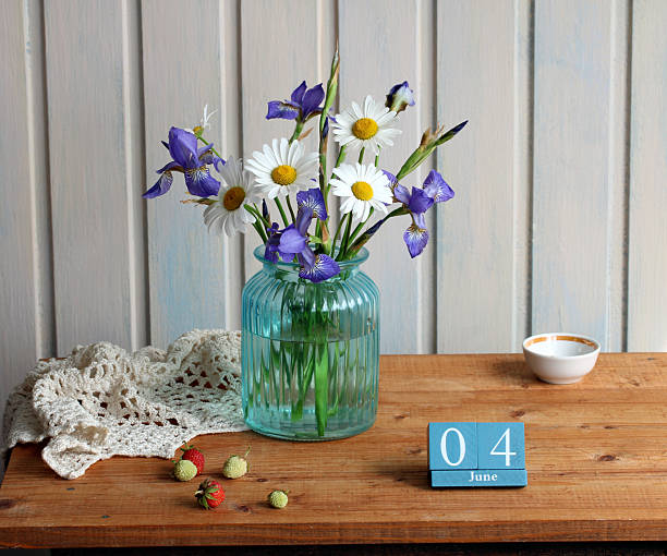 Spring still life featuring irises, daisies, calendar, strawberries on a wooden table. june 04