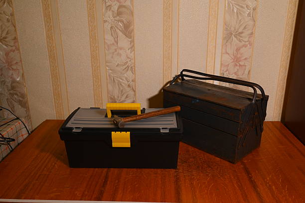 a modern black plastic case stands next to an old blue metal toolbox on a table with a time worn hammer with a wooden handle lying on top