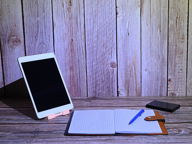 modern desktop with an open notebook and stationery under cold lighting against a wooden wall background emphasizing the texture of the materials