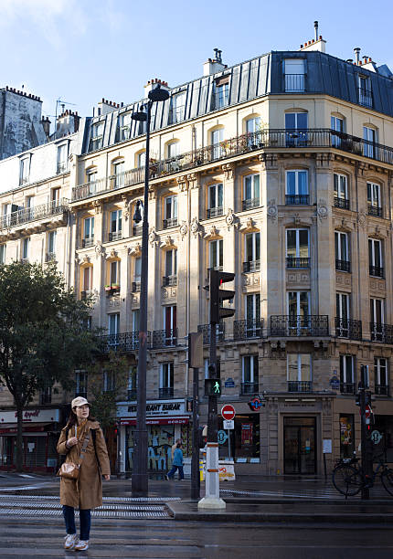 Paris, France - October 26, 2025: A woman crosses Avenue de la République (11th arrondissement) in the rain; the intersection also includes Avenue  Parmentier and Rue Oberkampf.