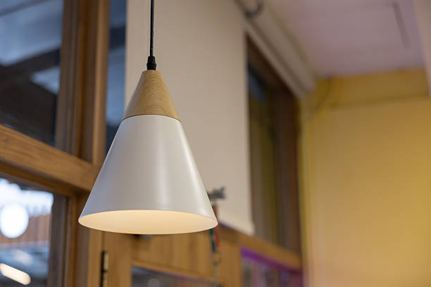 A white lamp with a wooden base hangs from the ceiling. The lamp is lit up and casts a warm glow on the room. The light is shining through the window, creating a cozy atmosphere