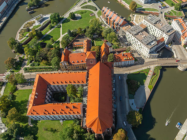 Aerial drone view of Wroclaw Old Town and the Oder River in Wroclaw, Poland. The cityscape features historic architecture, red roof buildings, cathedral landmarks, green riverside areas, and a vibrant urban landscape under a clear blue sky. Popular European travel destination showcasing cultural heritage, tourism, and scenic city panorama, captured on a sunny day. River Oder (Polish: Odra) and The St. John the Baptist Archcathedral (Polish: Archikatedra św. Jana Chrzciciela) The photo is taken with DJI Mavic 3 Drone