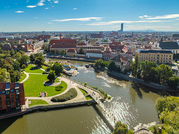 Aerial drone view of Wroclaw Old Town and the Oder River in Wroclaw, Poland. The cityscape features historic architecture, red roof buildings, cathedral landmarks, green riverside areas, and a vibrant urban landscape under a clear blue sky. Popular European travel destination showcasing cultural heritage, tourism, and scenic city panorama, captured on a sunny day. River Oder (Polish: Odra) and The St. John the Baptist Archcathedral (Polish: Archikatedra św. Jana Chrzciciela) The photo is taken with DJI Mavic 3 Drone