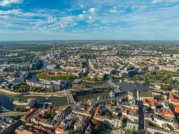 Aerial drone view of Wroclaw Old Town and the Oder River in Wroclaw, Poland. The cityscape features historic architecture, red roof buildings, cathedral landmarks, green riverside areas, and a vibrant urban landscape under a clear blue sky. Popular European travel destination showcasing cultural heritage, tourism, and scenic city panorama, captured on a sunny day. River Oder (Polish: Odra) and The St. John the Baptist Archcathedral (Polish: Archikatedra św. Jana Chrzciciela) The photo is taken with DJI Mavic 3 Drone