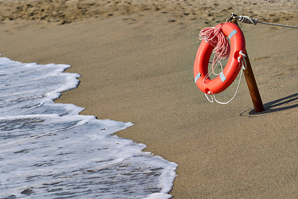 Orange lifebuoy hanging on a wooden post at the edge of the sea, providing safety and security on the beach