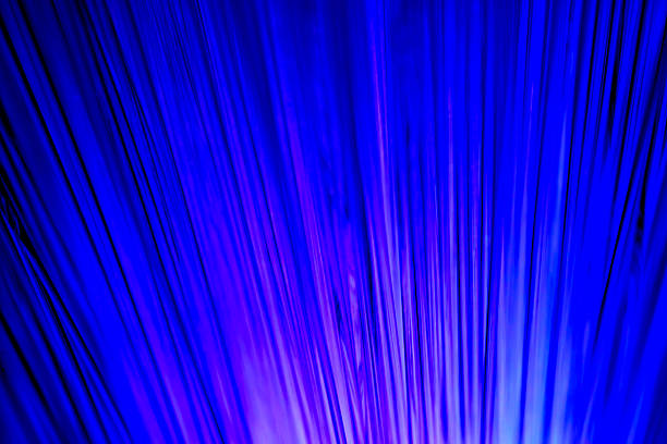 Close-up view of optical fiber cables glowing with blue light against a solid black background, creating an abstract pattern of soft, circular bokeh highlights and bursts of brighter illumination. The image captures the essence of data transmission and digital connectivity through luminous strands that evoke streams of information flowing in a high-tech environment. Ideal for illustrating concepts in telecommunications, internet infrastructure, big data, AI, and futuristic innovation in business and science publications. The horizontal composition emphasizes the complexity and beauty of fiber optic technology without any people or identifiable objects, focusing on the ethereal, glowing orbs that suggest speed and global communication networks. Suitable for editorial use in articles on digital transformation, cybersecurity, and engineering advancements.