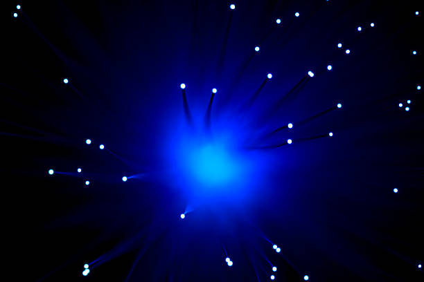 Close-up view of optical fiber cables glowing with blue light against a solid black background, creating an abstract pattern of soft, circular bokeh highlights and bursts of brighter illumination. The image captures the essence of data transmission and digital connectivity through luminous strands that evoke streams of information flowing in a high-tech environment. Ideal for illustrating concepts in telecommunications, internet infrastructure, big data, AI, and futuristic innovation in business and science publications. The horizontal composition emphasizes the complexity and beauty of fiber optic technology without any people or identifiable objects, focusing on the ethereal, glowing orbs that suggest speed and global communication networks. Suitable for editorial use in articles on digital transformation, cybersecurity, and engineering advancements.