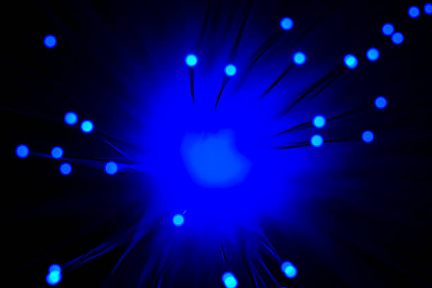 Close-up view of optical fiber cables glowing with blue light against a solid black background, creating an abstract pattern of soft, circular bokeh highlights and bursts of brighter illumination. The image captures the essence of data transmission and digital connectivity through luminous strands that evoke streams of information flowing in a high-tech environment. Ideal for illustrating concepts in telecommunications, internet infrastructure, big data, AI, and futuristic innovation in business and science publications. The horizontal composition emphasizes the complexity and beauty of fiber optic technology without any people or identifiable objects, focusing on the ethereal, glowing orbs that suggest speed and global communication networks. Suitable for editorial use in articles on digital transformation, cybersecurity, and engineering advancements.