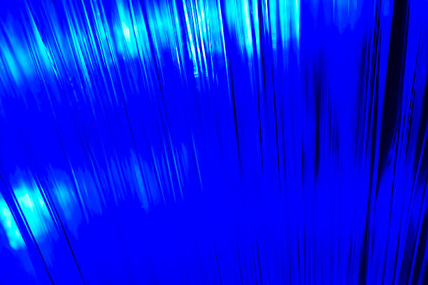 Close-up view of optical fiber cables glowing with blue light against a solid black background, creating an abstract pattern of soft, circular bokeh highlights and bursts of brighter illumination. The image captures the essence of data transmission and digital connectivity through luminous strands that evoke streams of information flowing in a high-tech environment. Ideal for illustrating concepts in telecommunications, internet infrastructure, big data, AI, and futuristic innovation in business and science publications. The horizontal composition emphasizes the complexity and beauty of fiber optic technology without any people or identifiable objects, focusing on the ethereal, glowing orbs that suggest speed and global communication networks. Suitable for editorial use in articles on digital transformation, cybersecurity, and engineering advancements.