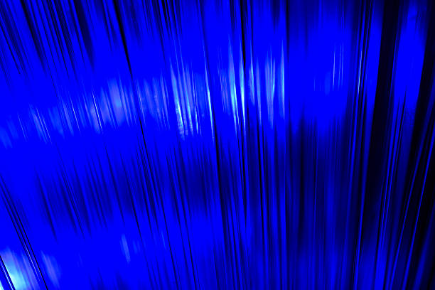 Close-up view of optical fiber cables glowing with blue light against a solid black background, creating an abstract pattern of soft, circular bokeh highlights and bursts of brighter illumination. The image captures the essence of data transmission and digital connectivity through luminous strands that evoke streams of information flowing in a high-tech environment. Ideal for illustrating concepts in telecommunications, internet infrastructure, big data, AI, and futuristic innovation in business and science publications. The horizontal composition emphasizes the complexity and beauty of fiber optic technology without any people or identifiable objects, focusing on the ethereal, glowing orbs that suggest speed and global communication networks. Suitable for editorial use in articles on digital transformation, cybersecurity, and engineering advancements.