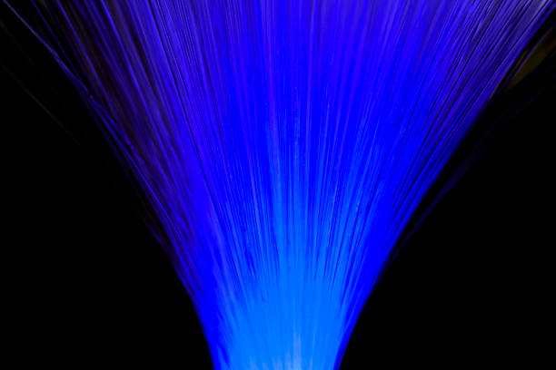 Close-up view of optical fiber cables glowing with blue light against a solid black background, creating an abstract pattern of soft, circular bokeh highlights and bursts of brighter illumination. The image captures the essence of data transmission and digital connectivity through luminous strands that evoke streams of information flowing in a high-tech environment. Ideal for illustrating concepts in telecommunications, internet infrastructure, big data, AI, and futuristic innovation in business and science publications. The horizontal composition emphasizes the complexity and beauty of fiber optic technology without any people or identifiable objects, focusing on the ethereal, glowing orbs that suggest speed and global communication networks. Suitable for editorial use in articles on digital transformation, cybersecurity, and engineering advancements.