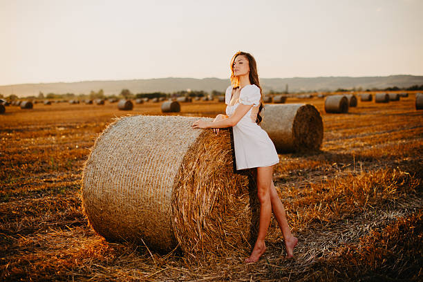 Woman in white dress standing on hay bale enjoying rural evening light