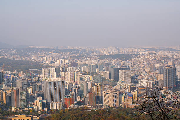 A panoramic view of Seoul, South Korea, from a hill just before sunset. The warm golden light bathes the cityscape, highlighting buildings, hills, and distant mountains. Ideal for themes such as urban landscapes, travel photography, city tourism, scenic viewpoints, sunset photography, and aerial-style city views.