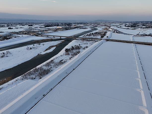 A snowy landscape with a river and a bridge in the background. The sky is a mix of blue and orange, creating a serene and peaceful atmosphere