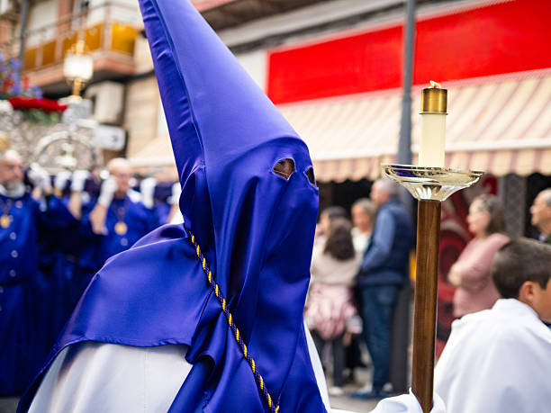 Nazareno wearing a purple capirote and holding a candle during a religious procession at Holy Week