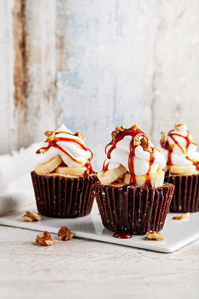 Delicious homemade chocolate muffin topped with fresh banana slices, fluffy whipped cream, walnuts, and sweet caramel sauce on a rustic plate.
