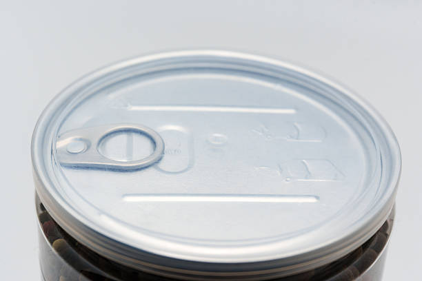 A close view of a can lid with a pull tab is resting on a jar filled with food. The lid shows clear markings and smooth surfaces.