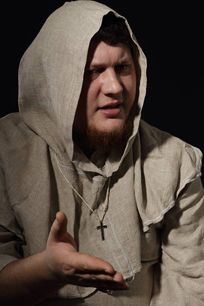 Christian monk in black robe looking up and praying to God with arms outstretched. Costume.