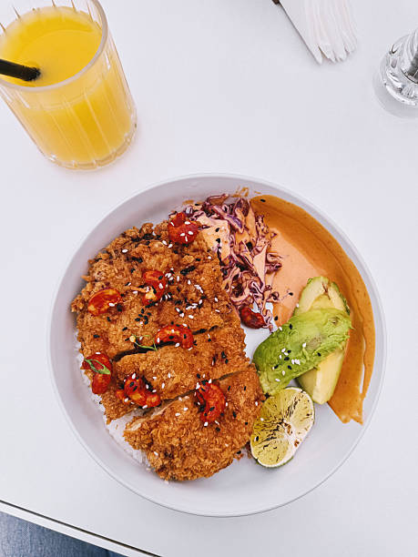 Overhead view of crispy breaded chicken served with rice, avocado, cabbage, spicy cashew topping and sauce