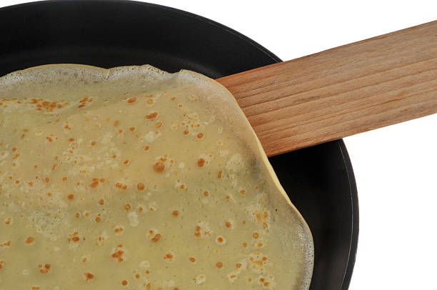 Cooked crepe with no toppings in a frying pan on a white background