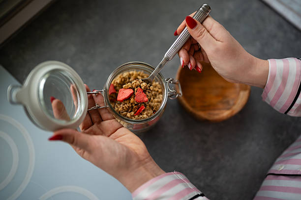 Woman scooping healthy granola from jar for breakfast