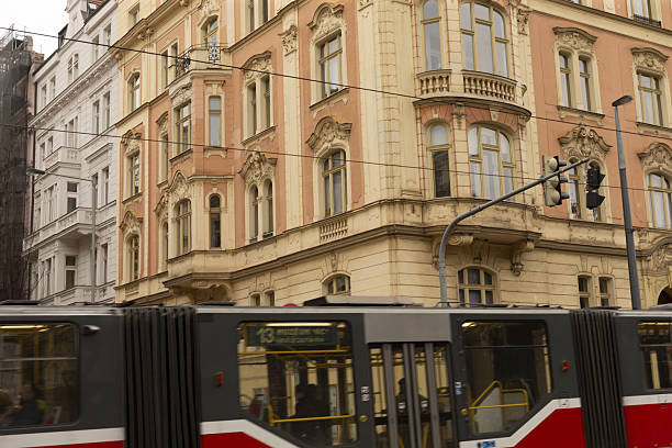 Historic european street with tram passing, ornate sandstone facades with wroughtiron balconies, tram rails, overhead cables and vintage street lamps, muted daylight