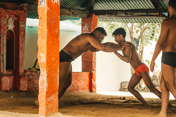 Varanasi, India - November 3, 2024: Two shirtless wrestlers grapple in a rustic open-air pit in Varanasi, India. The scene captures strength, focus, and culture within a red-orange shelter.