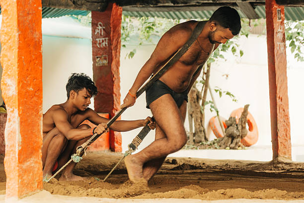 Varanasi, India - November 3, 2024: wo men wrestle on a dirt floor under a shelter with orange pillars in Varanasi, India. A traditional sport scene capturing culture, fitness, and focus.