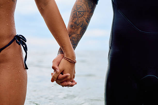 Couple sharing love and togetherness, holding hands with wet skin after surfing or swimming in the ocean