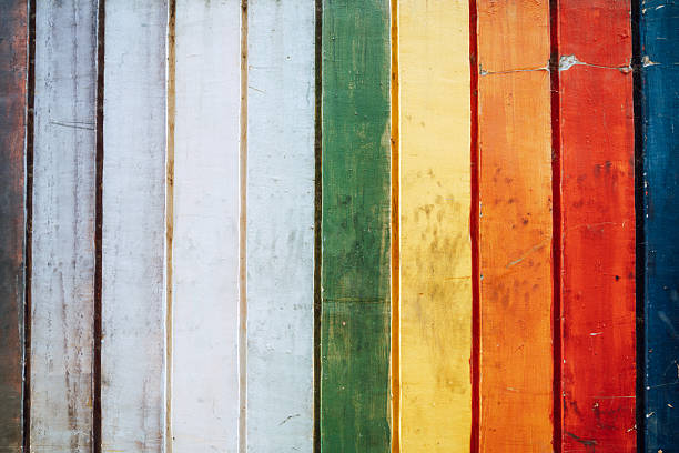 A close-up of vertical, weathered wooden planks painted in a rainbow of colors. Rich textures and bold colors create a vibrant, graphic background with a rustic, artistic feel.